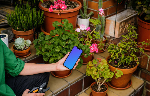 Main féminine tenant un iPhone 13 mockup dans un jardin