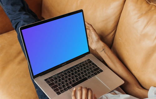 User on a leather sofa holding a MacBook Pro mockup