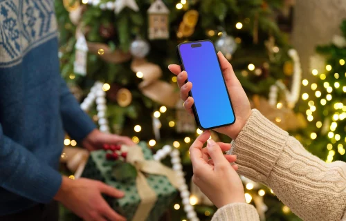 Femme tenant un iPhone mockup à côté du sapin de Noël