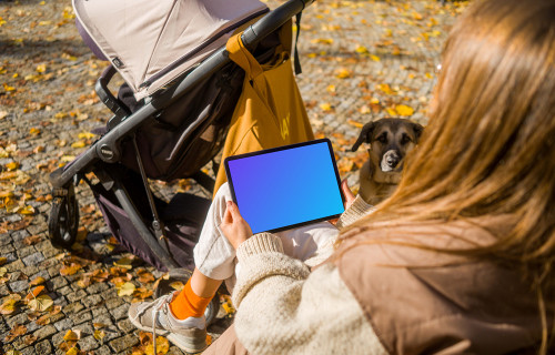 Woman sitting and holding an iPad Air in autumn themed park mockup