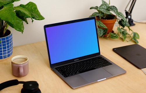 Grey MacBook Pro mockup with a coffee mug and an iPad at the side.