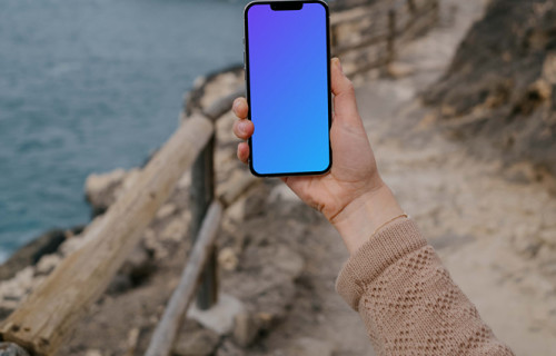 iPhone 13 Pro mockup held up beside the ocean