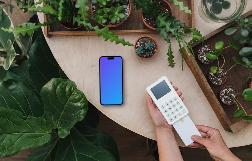 Payment terminal and an iPhone mockup surrounded by plants