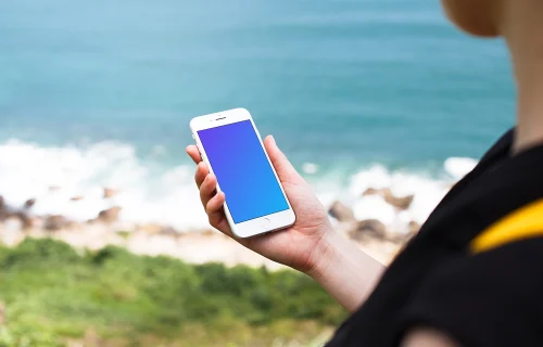 Tenant un iPhone 7 mockup à côté de l'océan