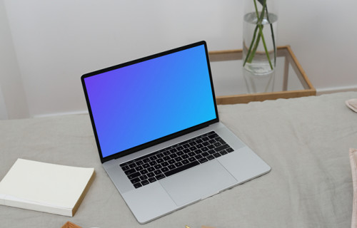 MacBook mockup sur un lit avec une cruche et de la céramique sur un plateau en bois et un carnet de notes à côté