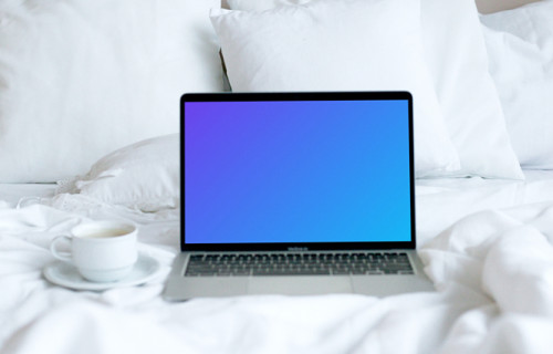 MacBook mockup placé sur un lit blanc avec une tasse de café à côté
