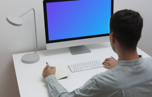 Mockup d'un homme utilisant un iMac sur une table blanche dans un bureau à domicile