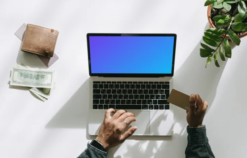 Mockup d'un utilisateur faisant du shopping sur un MacBook gris à côté de quelques billets et d'un portefeuille