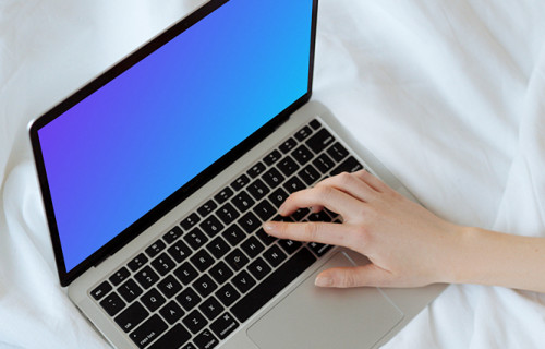 MacBook mockup sur un lit blanc avec un utilisateur tapant sur l'ordinateur portable
